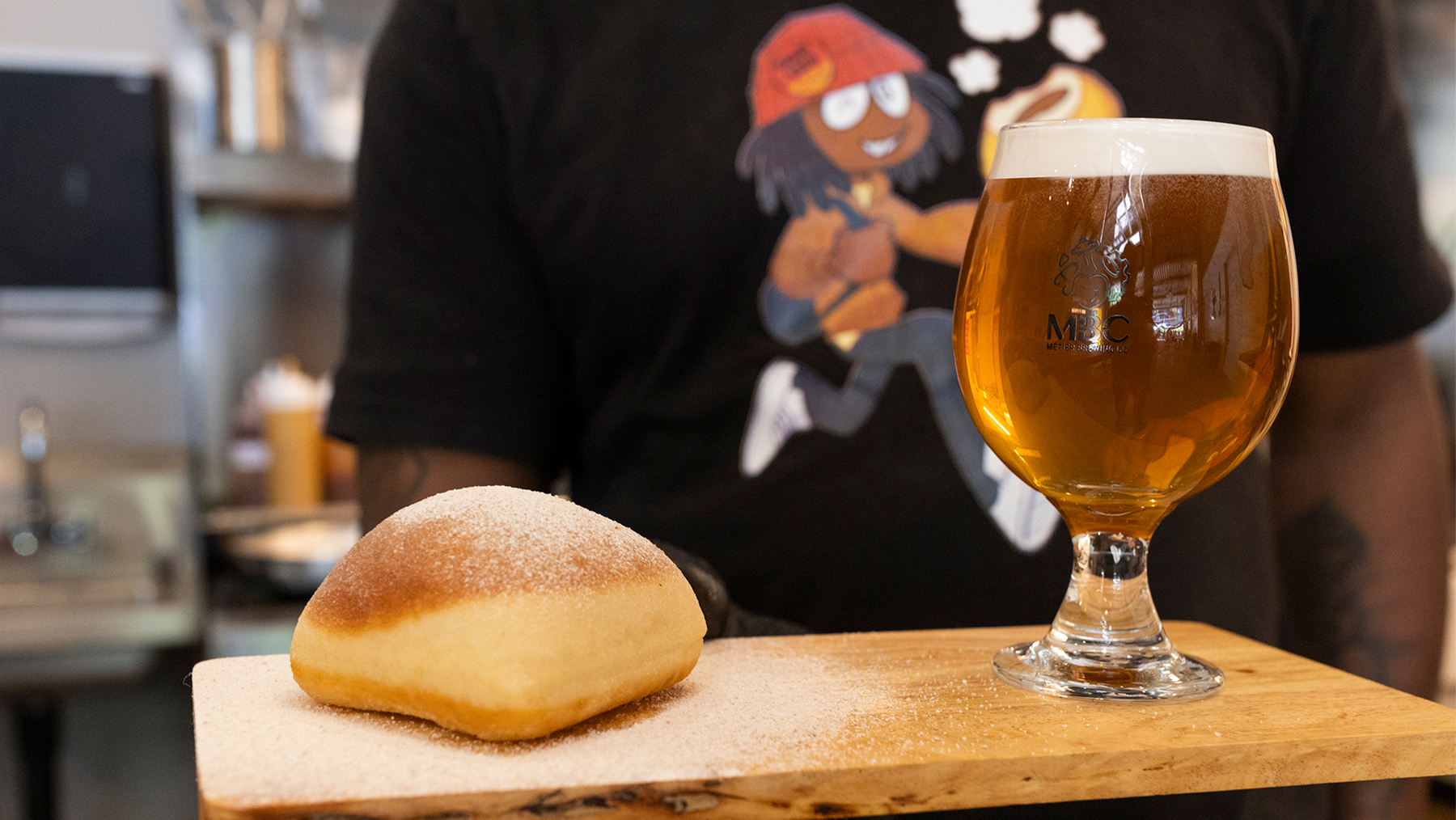 Short glass of honey-colored beer next to an Umami Kushi beignet