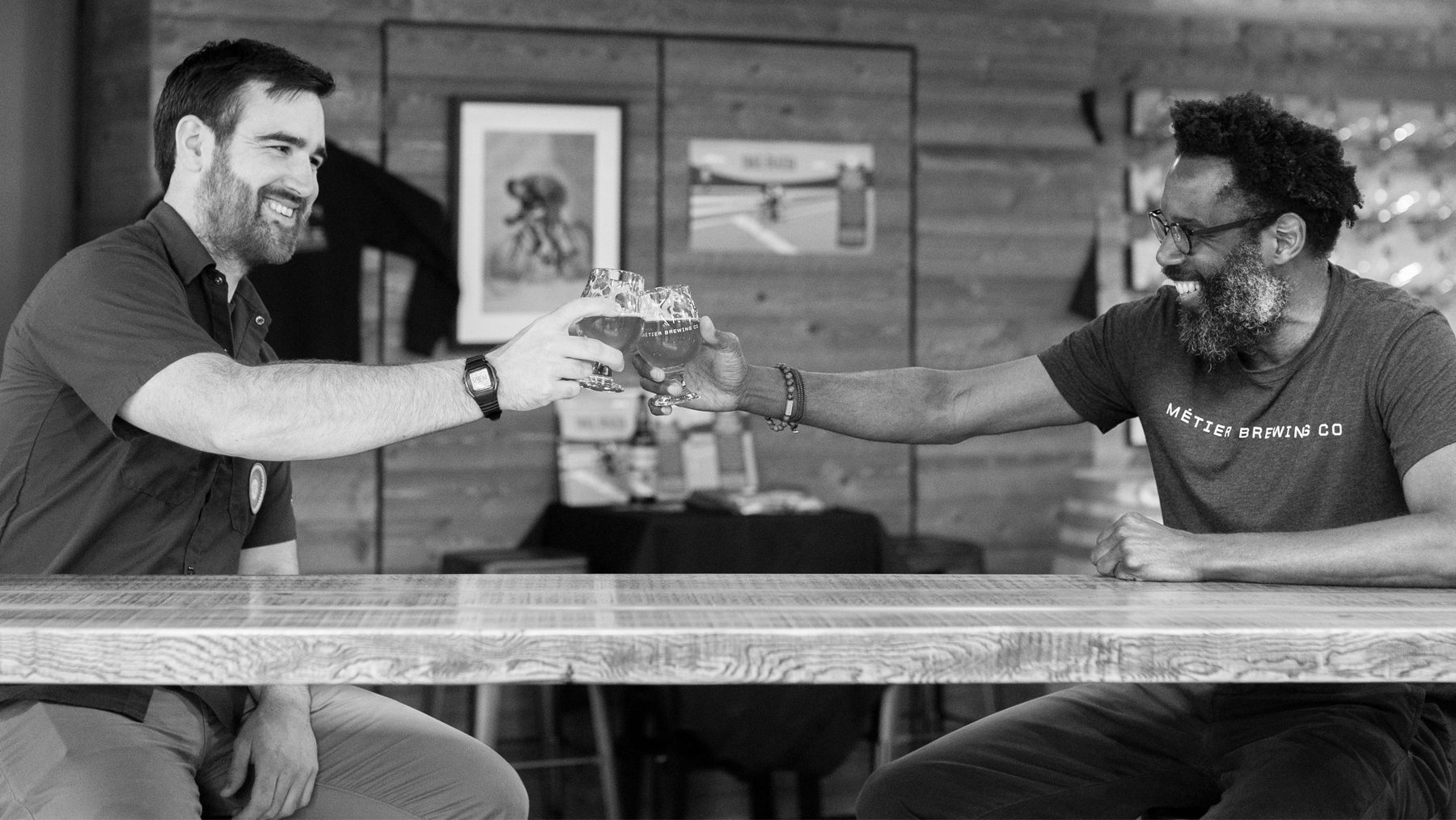 Black and white image of 2 MBC employees clinking glasses of beer together