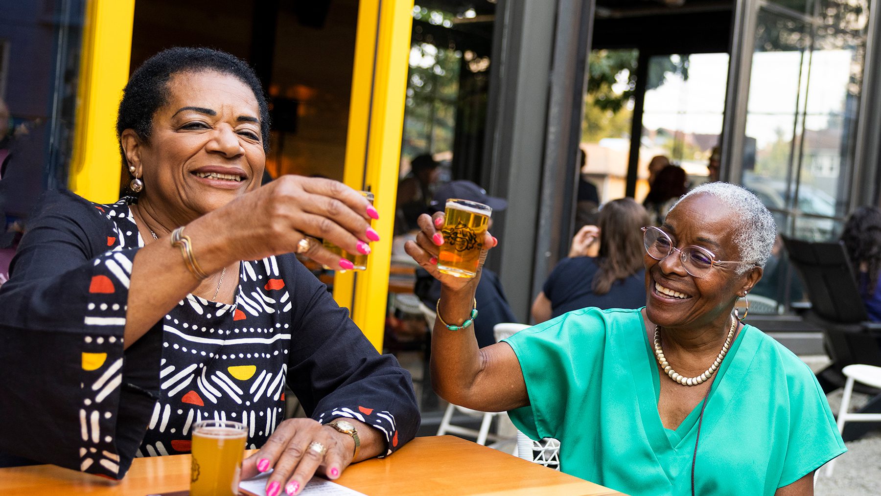 Two women raise small glasses of beer