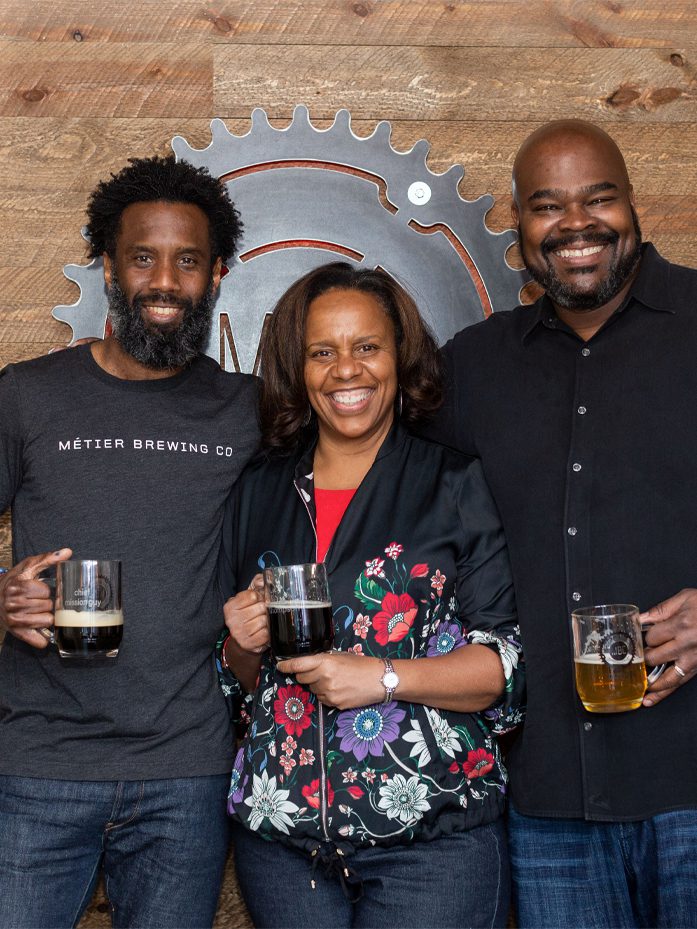 Rodney Hines, CEO, smiling and standing with two customers with glasses full of beer.
