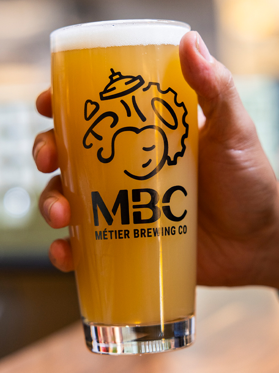 A hand holding a tall glass of MBC beer