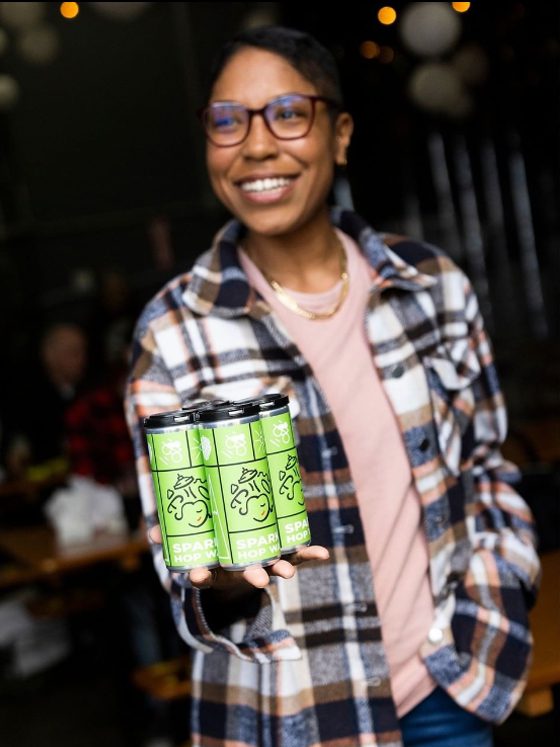 A person holding three cans of Metier's green 'Sparkling Hop Water' for the camera.