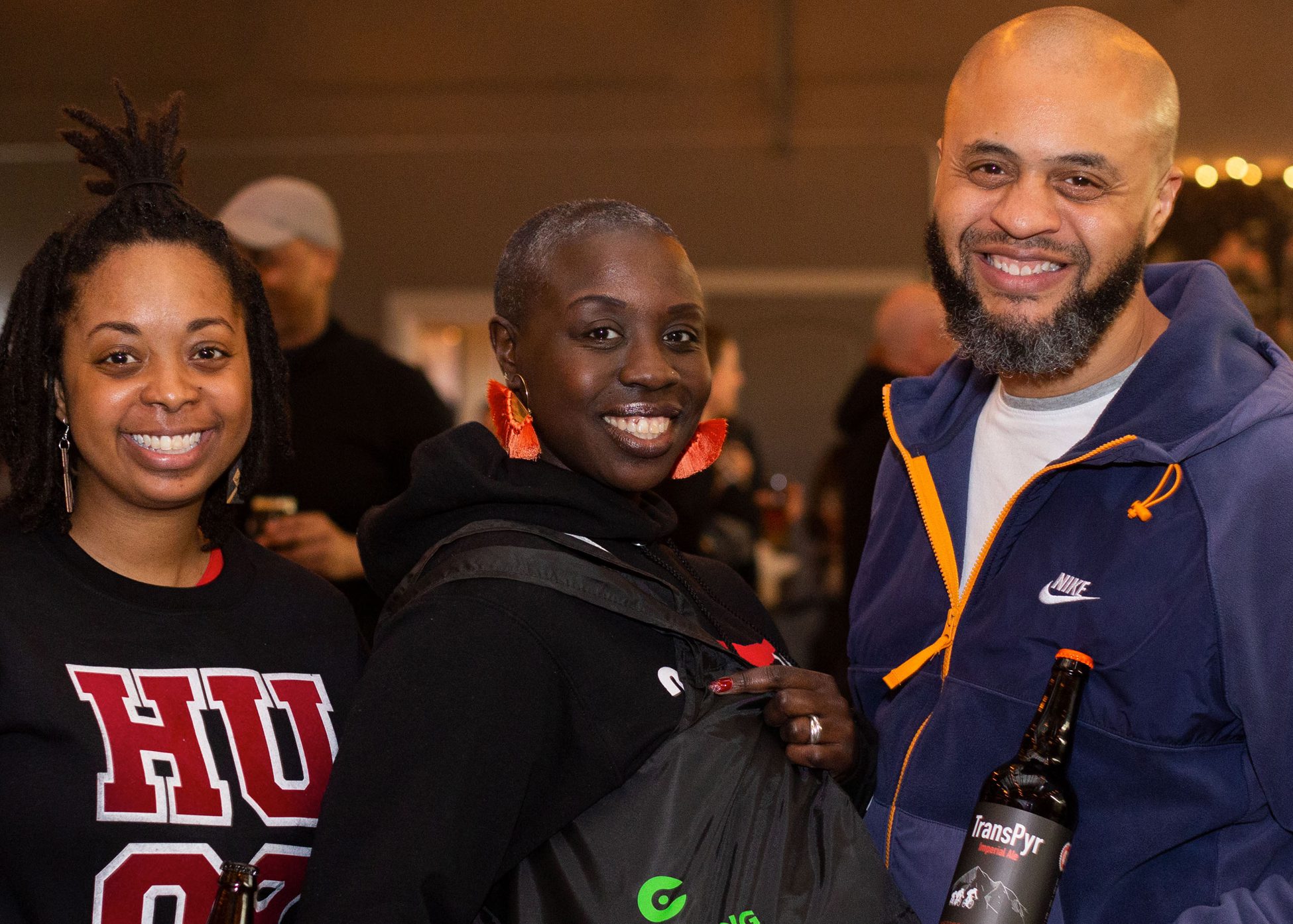 Three people smiling at the camera. One person is holding a TransPyr beer.