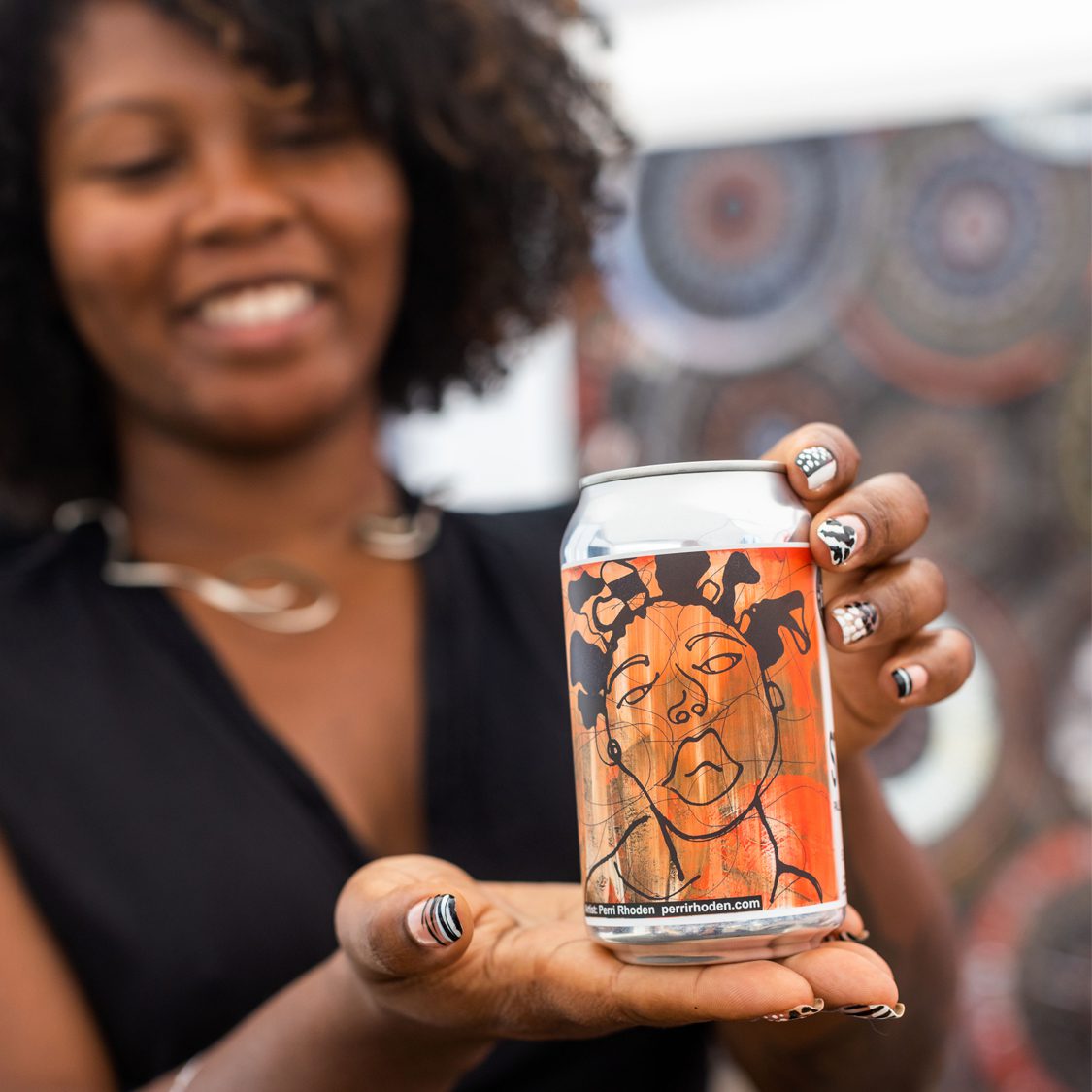 A person holding a Perri Rhoden beer in front of the camera.