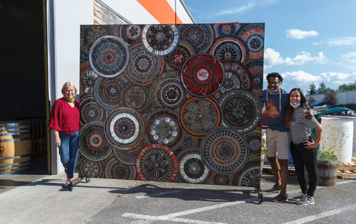 Rodney Hines, CEO, standing outside next to a huge piece of art with two community members
